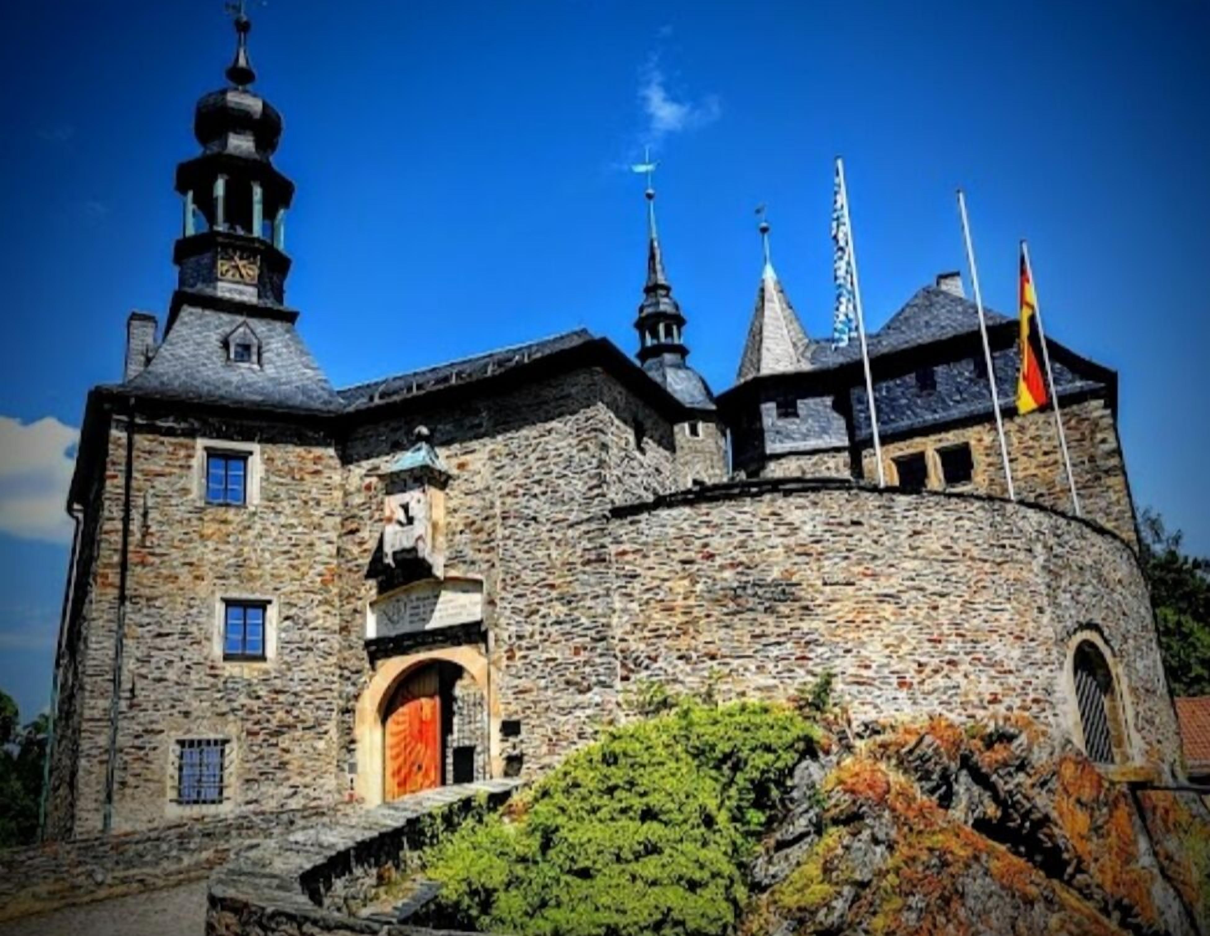 A historic stone building with a prominent clock tower, arched windows, and flags.