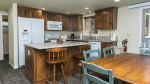 A kitchen with wooden cabinets, a granite countertop, a white refrigerator, a microwave, a stove, and a dining table with chairs.