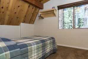 Un dormitorio con cama, ventana con vista a árboles y techo de madera.