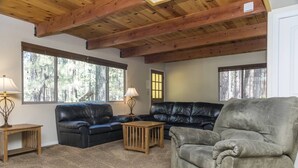 A living room with a wooden ceiling, two black leather sofas, a grey armchair, and a wooden coffee table.