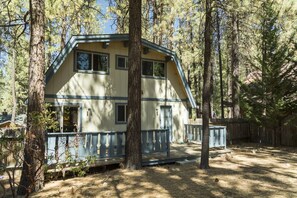 A two-story cabin with a balcony, surrounded by trees.