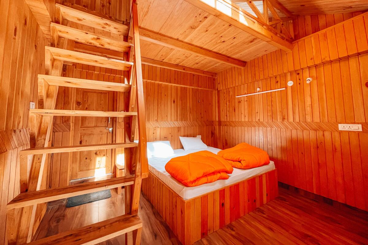 A wooden cabin room with a bed, a ladder, and a wooden ceiling.