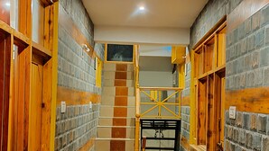 Un estrecho pasillo con puertas de madera y paredes de piedra, que conduce a una escalera y un pequeño cuarto con chimenea.