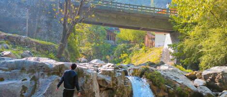A person standing on rocks near a waterfall with a bridge in the background.