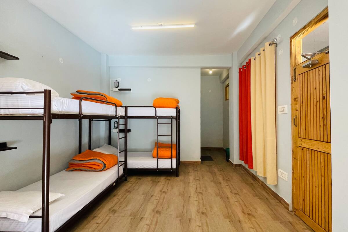 A dormitory room with bunk beds, a wooden floor, and a door with a red curtain.