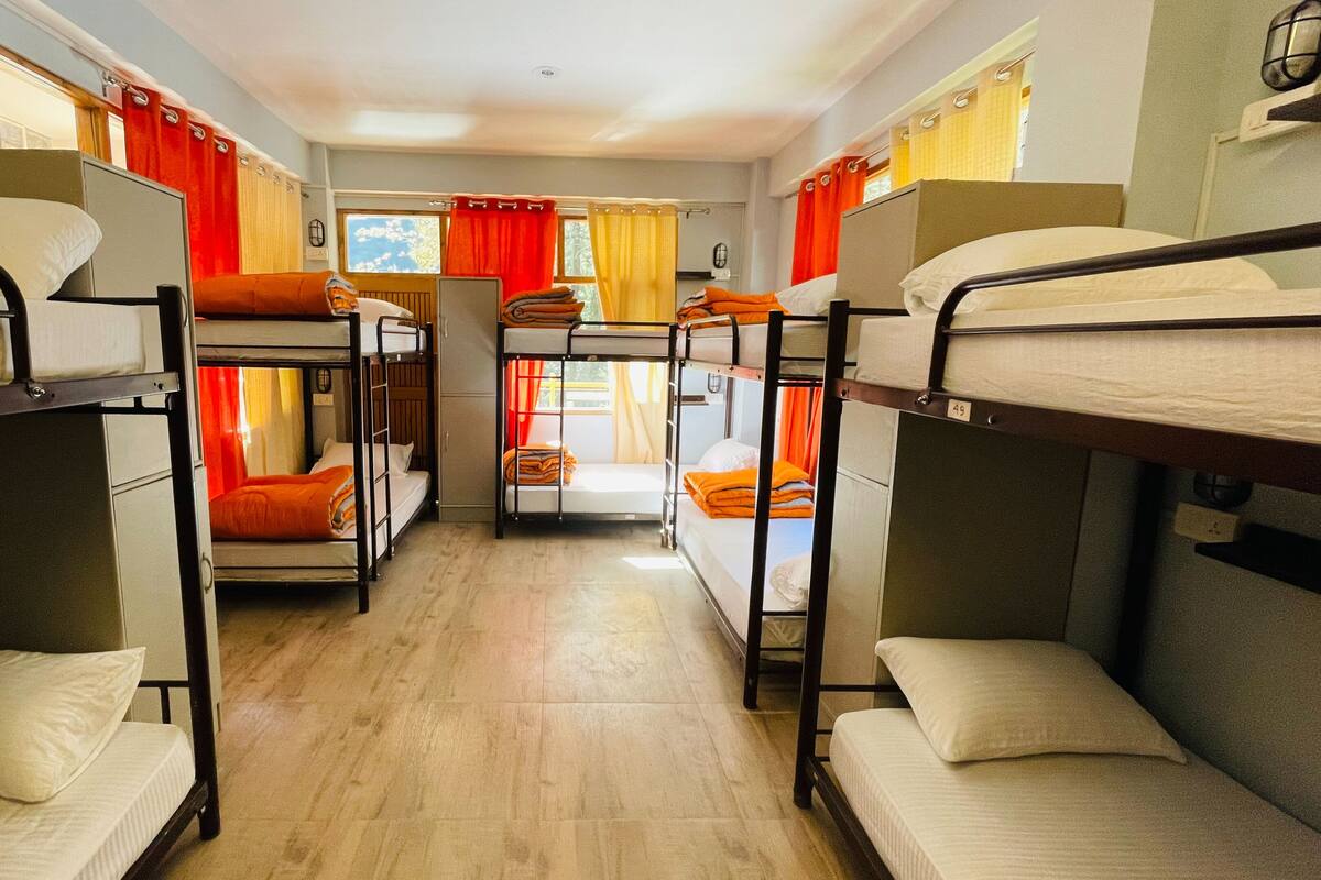A dormitory room with bunk beds, a wooden floor, and curtains.