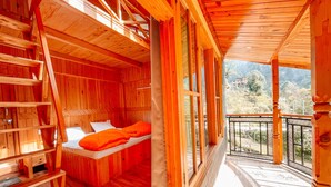 Una cabaña de madera con una cama en el altillo, una mesita y una escalera.