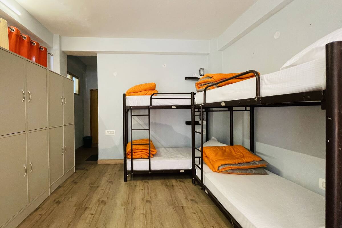 A dormitory room with bunk beds, a wardrobe, and a small door leading to another room.