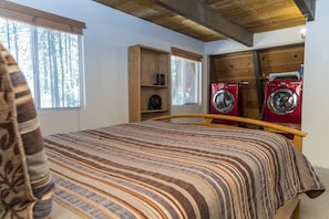 A bedroom with a bed, a wooden headboard, a window with a view of trees, and two red washing machines.