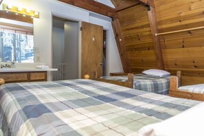 A room with two beds, a wooden ceiling, a mirror with lights, a window, and a door marked with a 'B'.