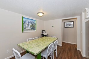 A dining area with a wooden table and white chairs, a ceiling light, and a framed picture on the wall.