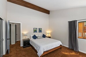 Een slaapkamer met een bed, nachtkastjes, een raam met gordijnen en een deur.
