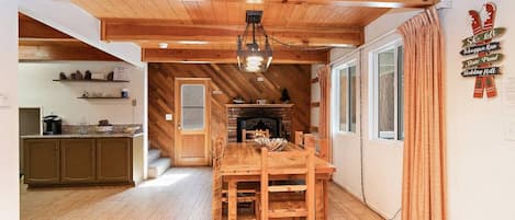 Un intérieur en bois comprenant une table à manger, des chaises, une cheminée et un coin cuisine.