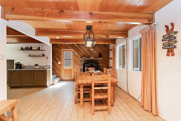 Een houten interieur met een eettafel, stoelen, een open haard en een keukenhoek.