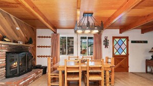 A cozy dining area with a brick fireplace, wooden dining table, and chairs.