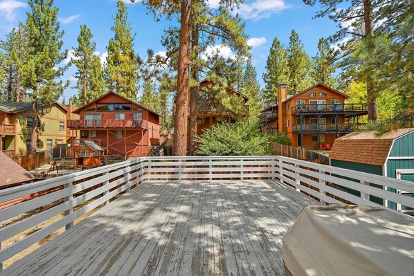A wooden deck with a white railing, surrounded by multi-story cabins with balconies, set in a forested area.