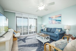 Ein Wohnzimmer mit einem blauen Sofa, einem Couchtisch, einem Fernseher und einem Balkon mit weißen Fensterläden.