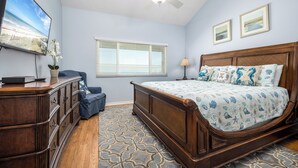 Un dormitorio con cama de madera, televisor en una cómoda, ventana con persianas y ventilador de techo.