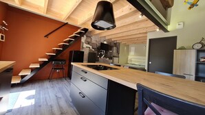 Uma cozinha moderna com escada de madeira, área de refeições e um pequeno quarto com cama e mesa de cabeceira.