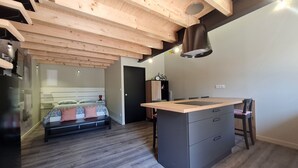 Quarto moderno com teto de madeira, cama com roupa de cama estampada, mesa de cabeceira e uma pequena escrivaninha com cadeira.