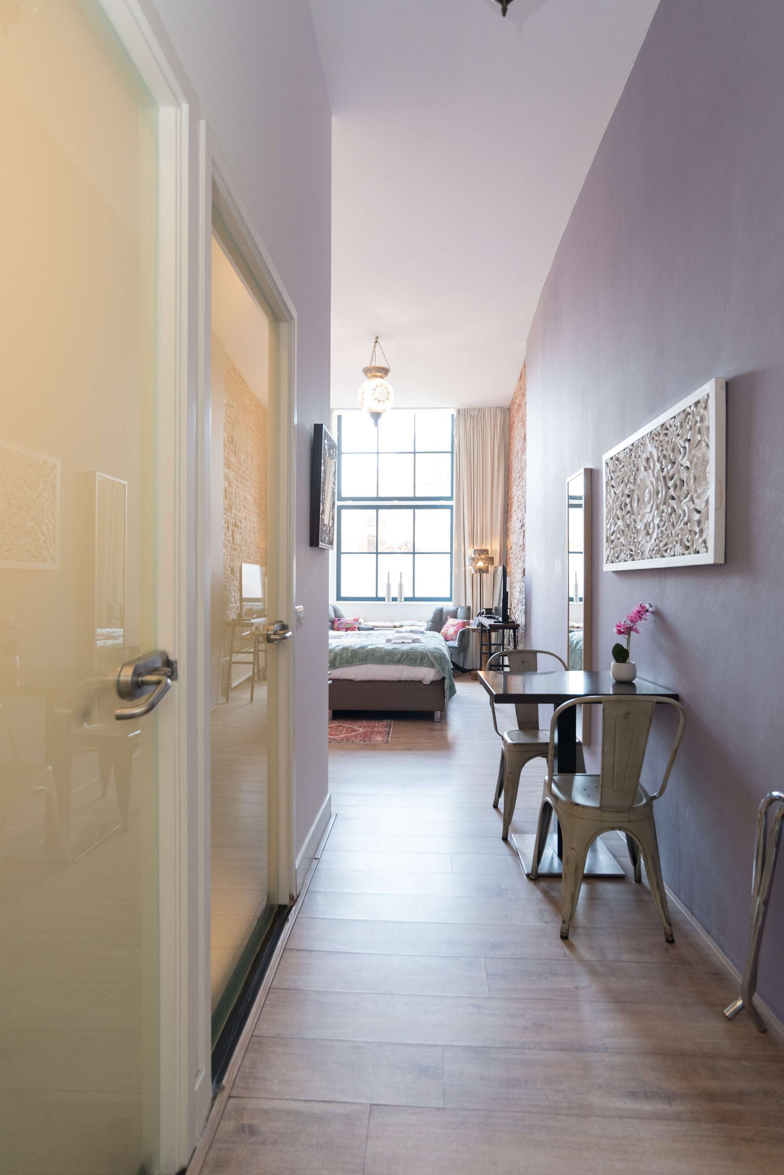 A hallway leading to a bedroom with a bed, a desk, and a chair.
