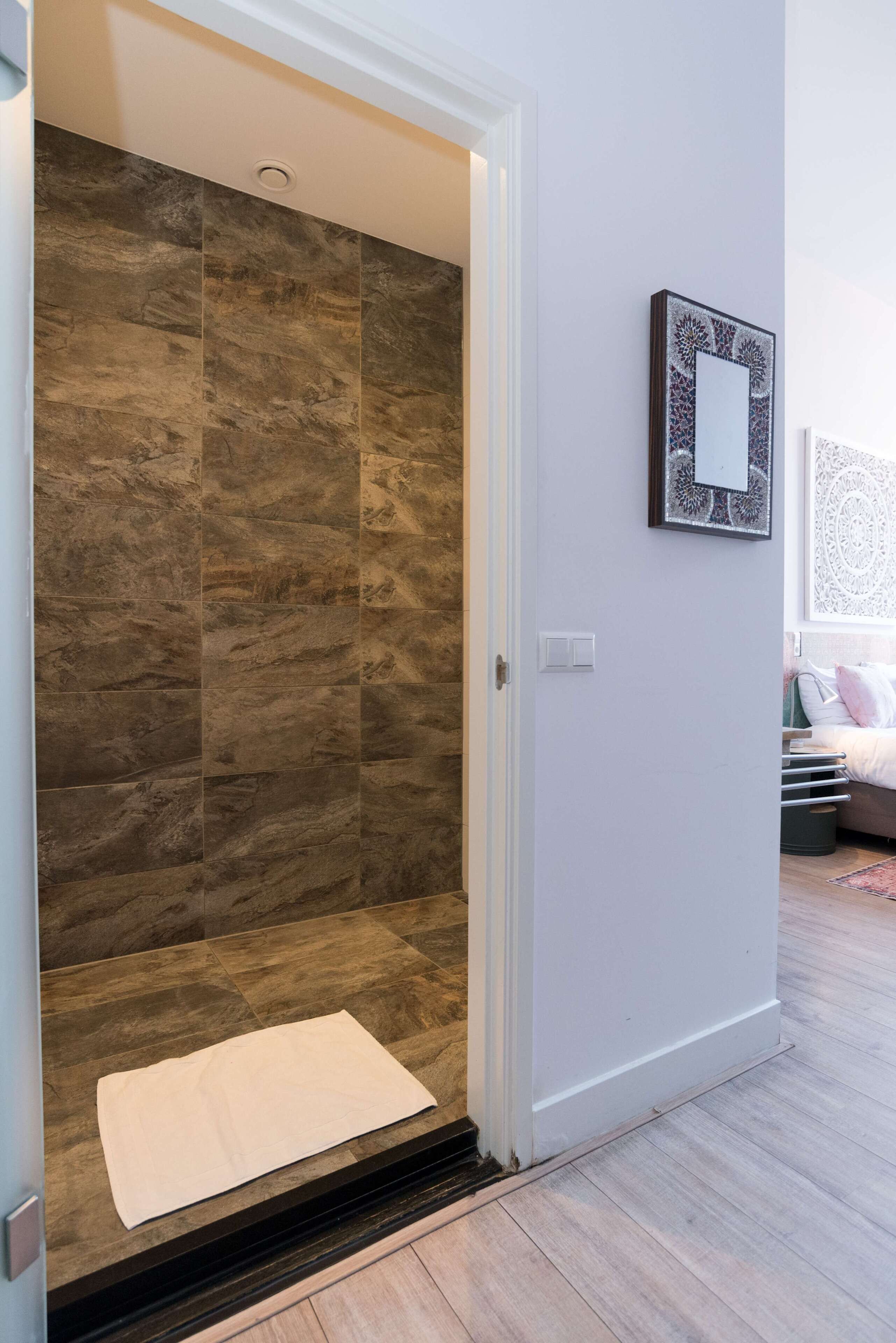 A shower area with a tiled wall, a white mat, and a framed picture on the wall.