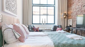 Een moderne hotelkamer met een groot raam, een bakstenen muur, een bed met kussens, een bijzettafeltje en een televisietoestel.