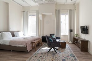 A bedroom with a bed, a desk, a chair, a TV, and a window. - 1001 Nights Boutique Lofts 1 (Haarlem)