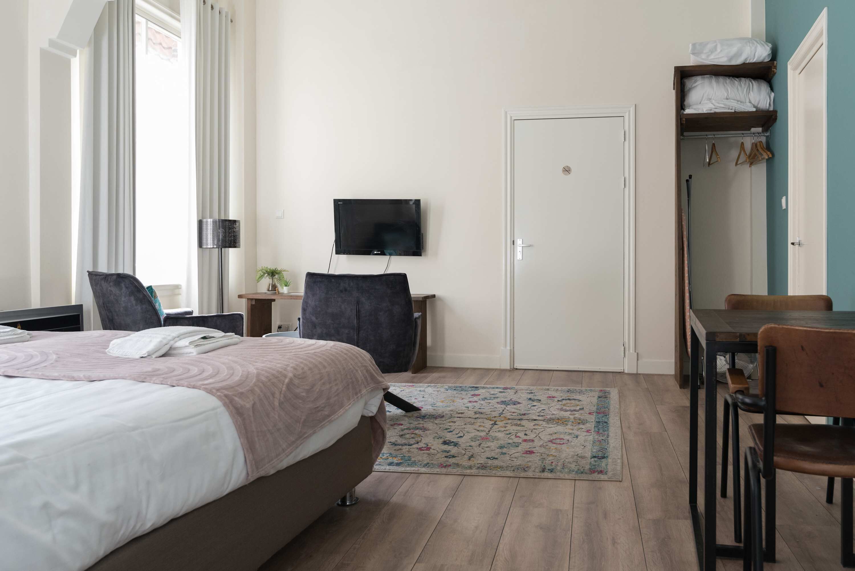 Een hotelkamer met een bed, bureau, stoel, televisie, kast en een deur.