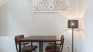 Un coin repas comprenant une table rectangulaire, quatre chaises, un panneau décoratif fixé au mur et un lampadaire.
