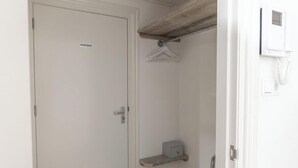 Une porte blanche avec une étiquette, une étagère en bois, un porte-manteau et un téléphone fixé au mur.
