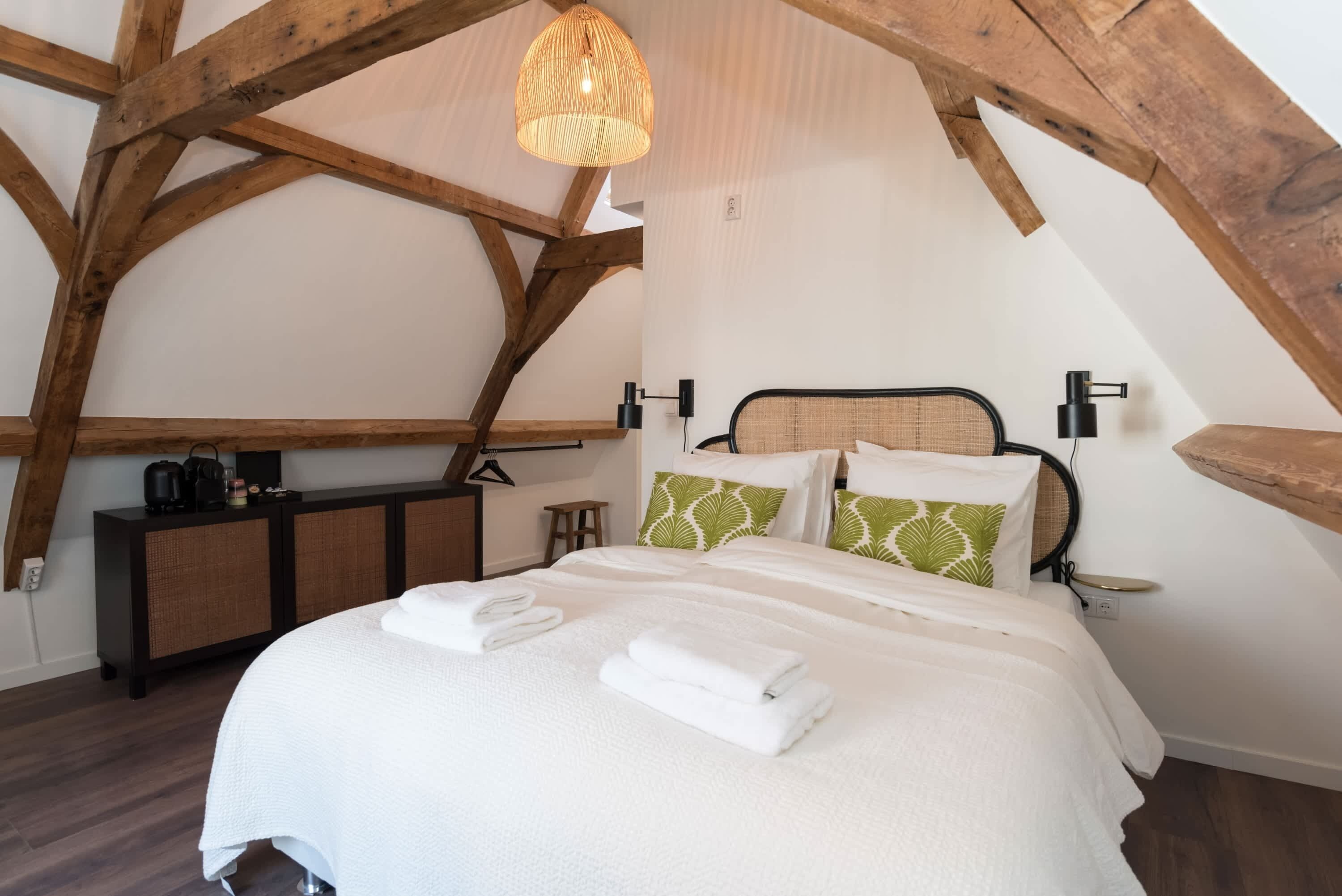 A bedroom with a bed, pillows, a bedside table, a hanging light fixture, and wooden beams.