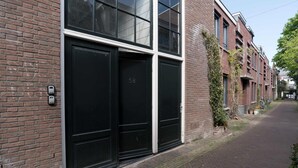 Ein Backsteinhaus mit großen schwarzen Türen, der Hausnummer '58' und einer schmalen gepflasterten Straße.
