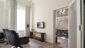 Ein modernes Wohnzimmer mit einem Flachbildfernseher, einem dunklen Sessel, einem Holztisch und einem farbenfrohen Teppich.