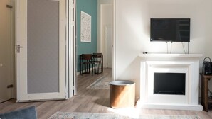 Ein Wohnzimmer mit grauem Sofa, einem gemusterten Teppich, einem Kamin und einem darüber montierten Fernseher.
