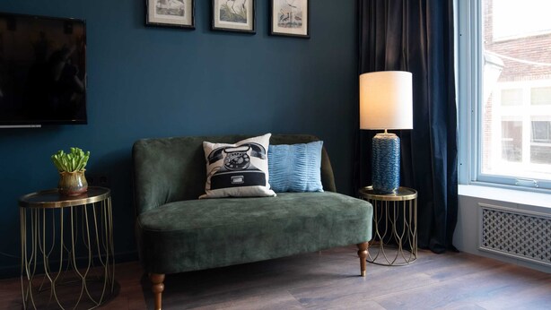 A living room with a green sofa, a side table with a lamp, and framed wall art.