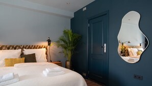 A bedroom with a bed, a potted plant, a door, and a mirror.