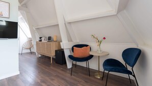 A modern loft bedroom with a sloped ceiling, a wooden floor, a desk with a chair, a small table with a vase, and two chairs. - Six Boutique Hotel - Luxury Quadruple Room (Haarlem)