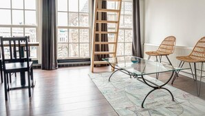 A modern room with a glass table, two wicker chairs, a wooden ladder, and large windows with curtains. - Oude advertentie Grote markt 19: The Square House (Haarlem)