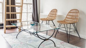 A room with a glass-top table, two wicker chairs, a wooden ladder, and a radiator. - Oude advertentie Grote markt 19: The Square House (Haarlem)
