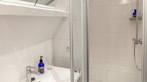 A modern bathroom with a glass shower enclosure, a white tiled wall, and a visible power outlet. - Oude advertentie Grote markt 19: The Square House (Haarlem)