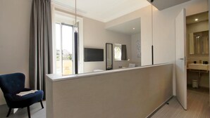 A modern hotel room with a desk, a chair, a TV, and a bathroom visible through an open door. - Vico Fashion District (Milan)