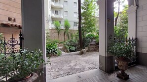 An entrance to a courtyard with a paved path, potted plants, and a gated area leading to a building with balconies. - Vico Fashion District (Milan)