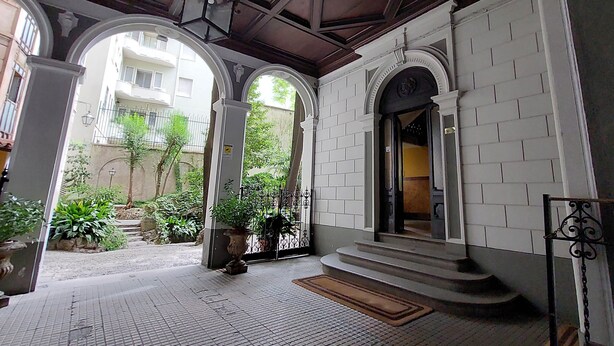 A covered entrance with white brick walls and arches, a tiled floor, and a small garden area with potted plants. - Vico Fashion District (Milan)