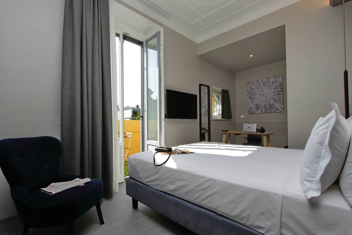 A hotel room with a bed, a chair, a desk, a television, and a window with curtains.
