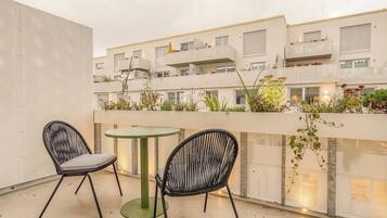 Un balcón con dos sillas y una mesa, con vista a un edificio con balcones y plantas.