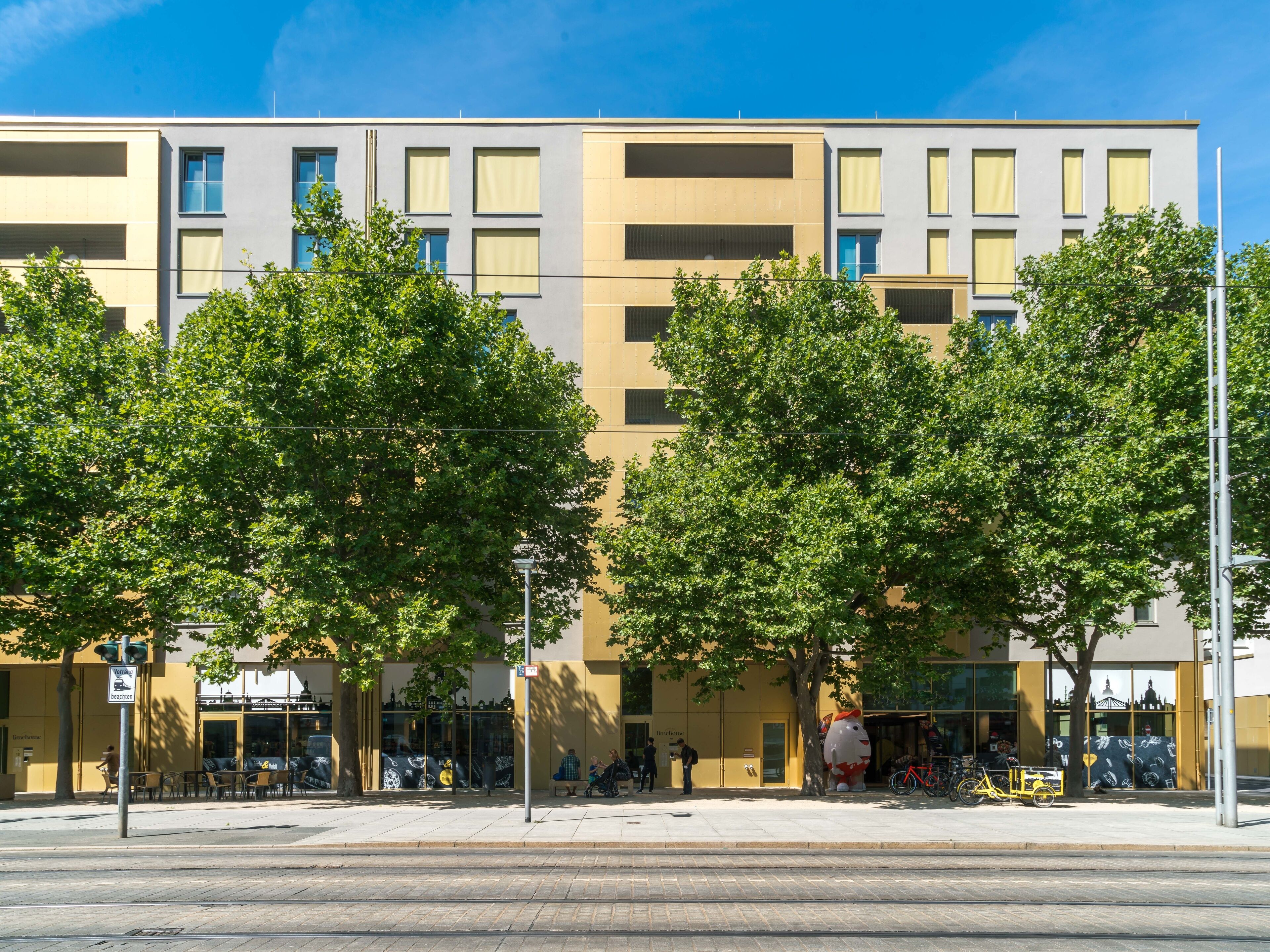 Un edificio moderno con varios pisos, ventanas grandes y fachada amarilla.