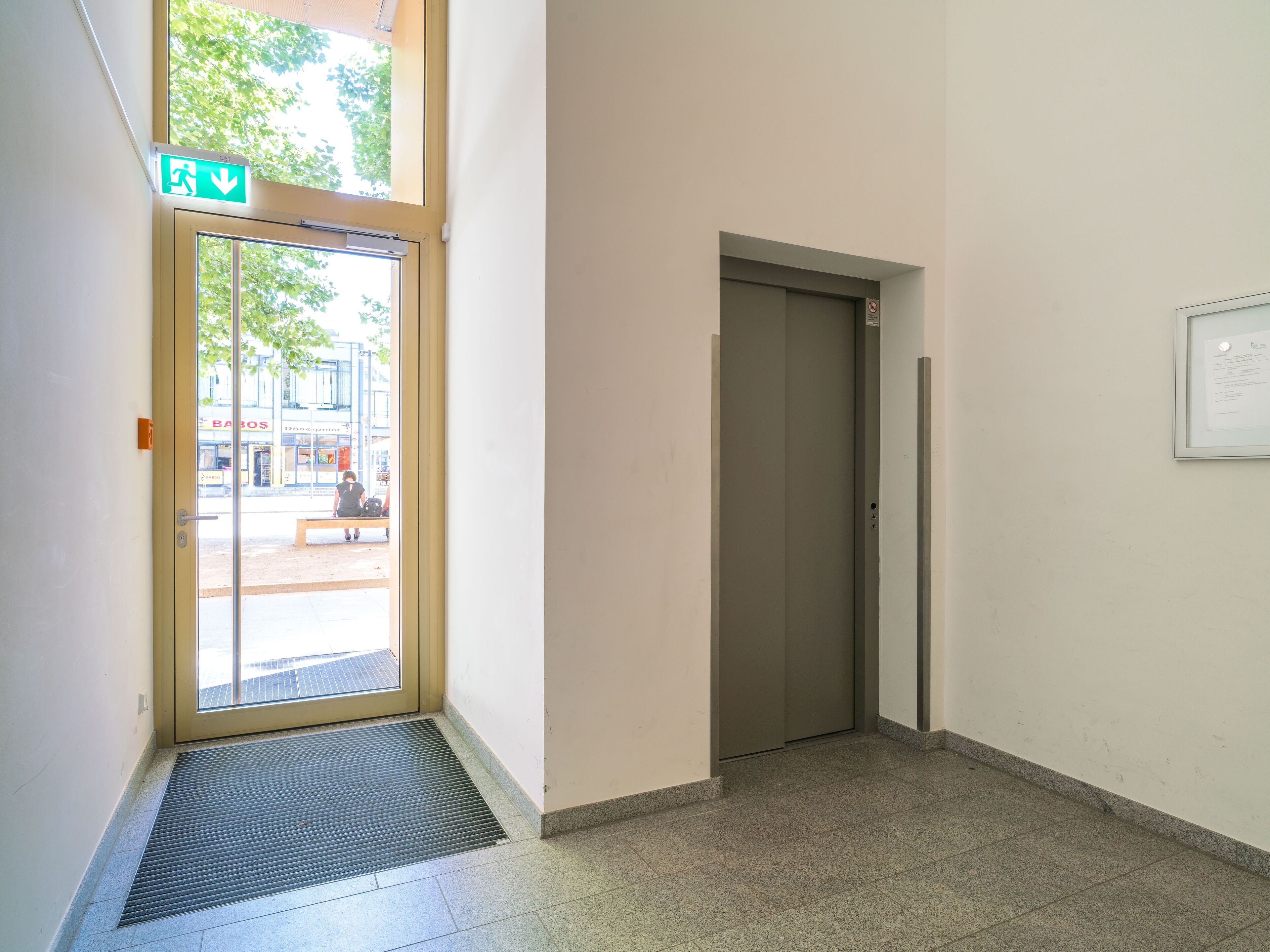 Ein Korridor mit einer Tür, einem Lüftungsgitter und einem Fenster mit Blick ins Freie.