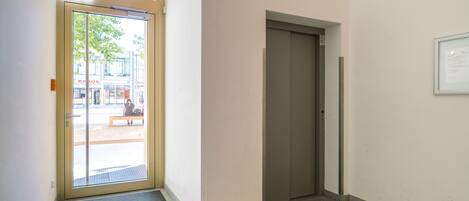 Ein Korridor mit einer Tür, einem Lüftungsgitter und einem Fenster mit Blick ins Freie.