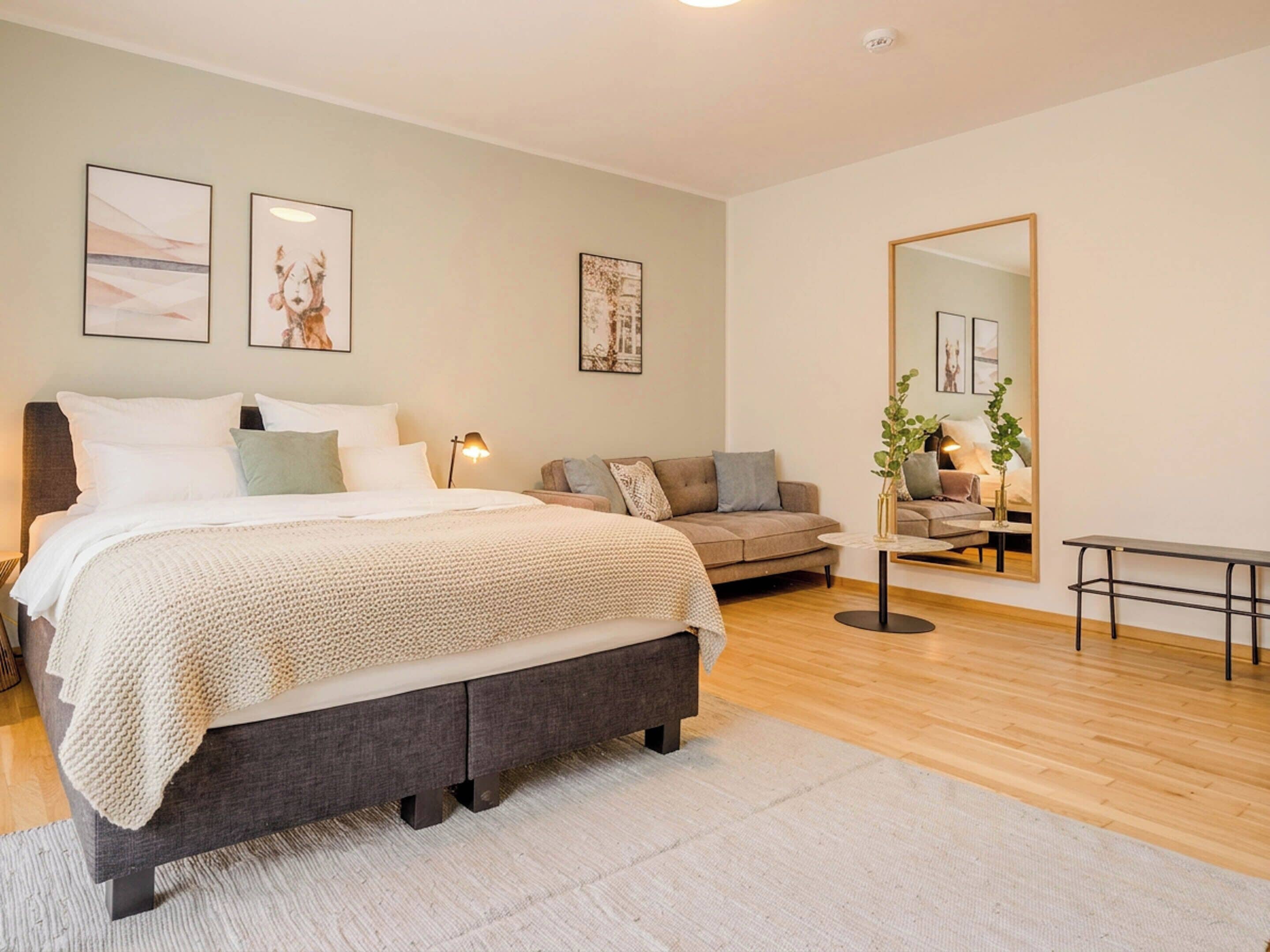 A modern bedroom with a large bed, a sofa, a small table, and a mirror.